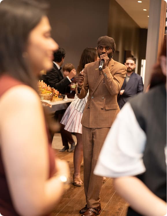 Man in a brown plaid suit speaking into a microphone at the A Cut Above showcase.