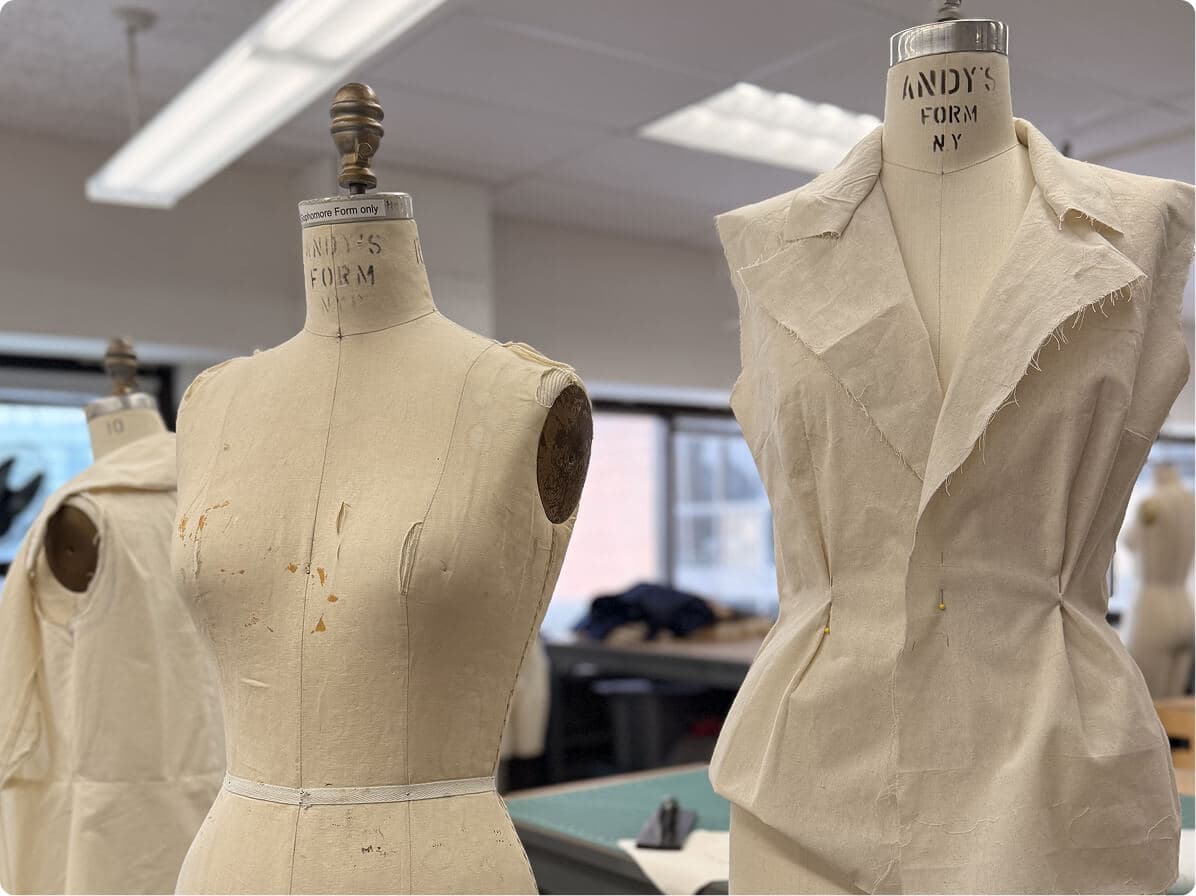 Two dress forms displaying an unfinished muslin jacket prototype in a fashion studio.