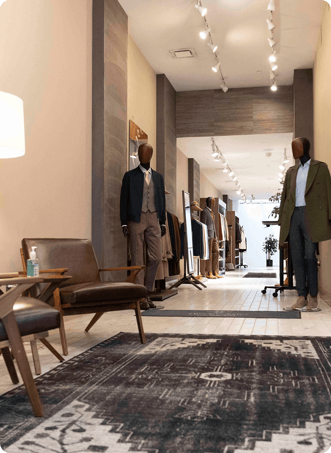 Tailoring showroom hallway with mannequins, clothing racks, and lounge chairs.