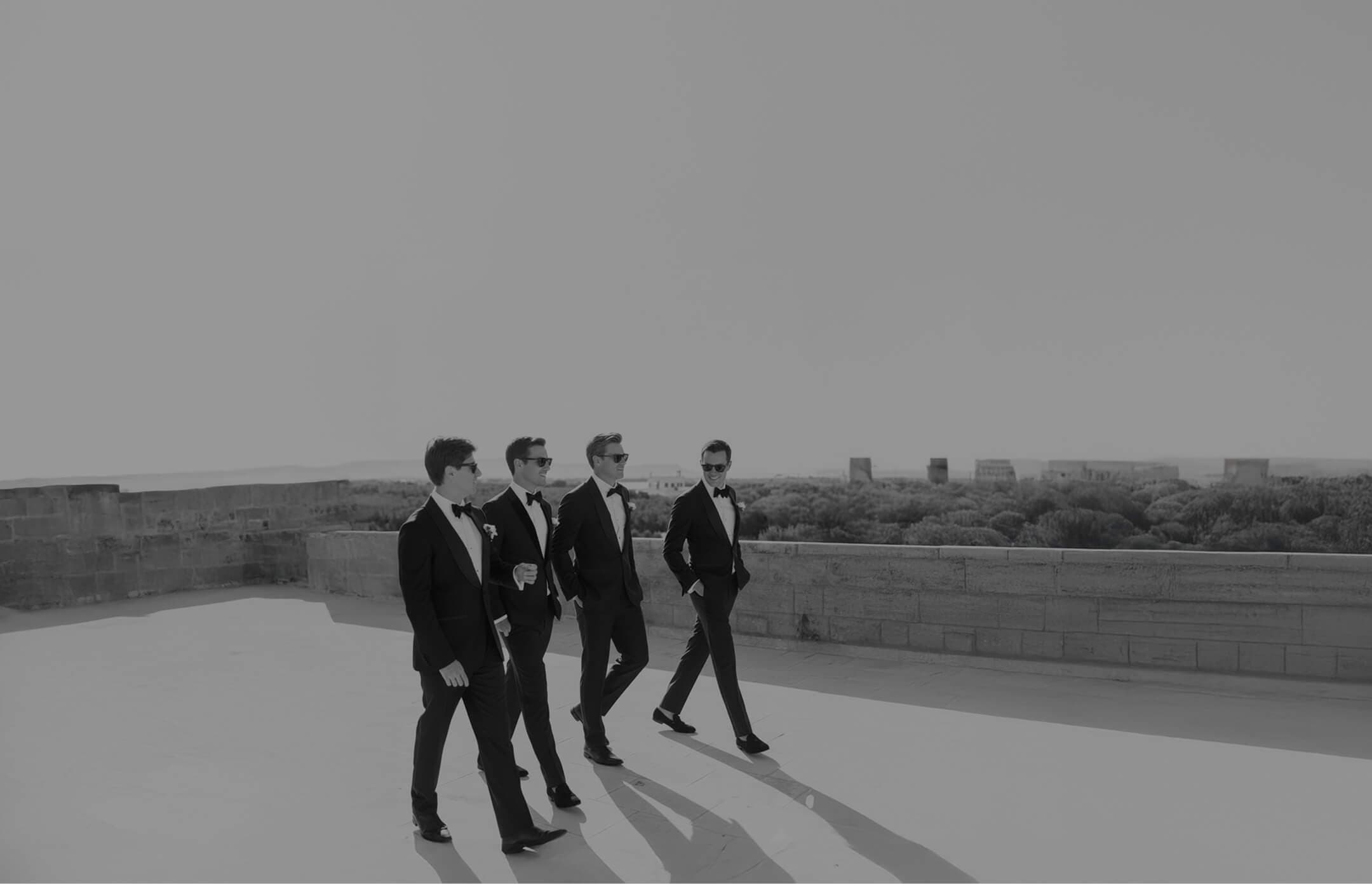 Groomsmen in black tuxedos walking across a rooftop.