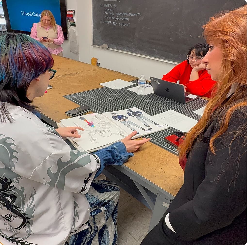 Fashion students reviewing jacket sketches and design concepts around a studio table.