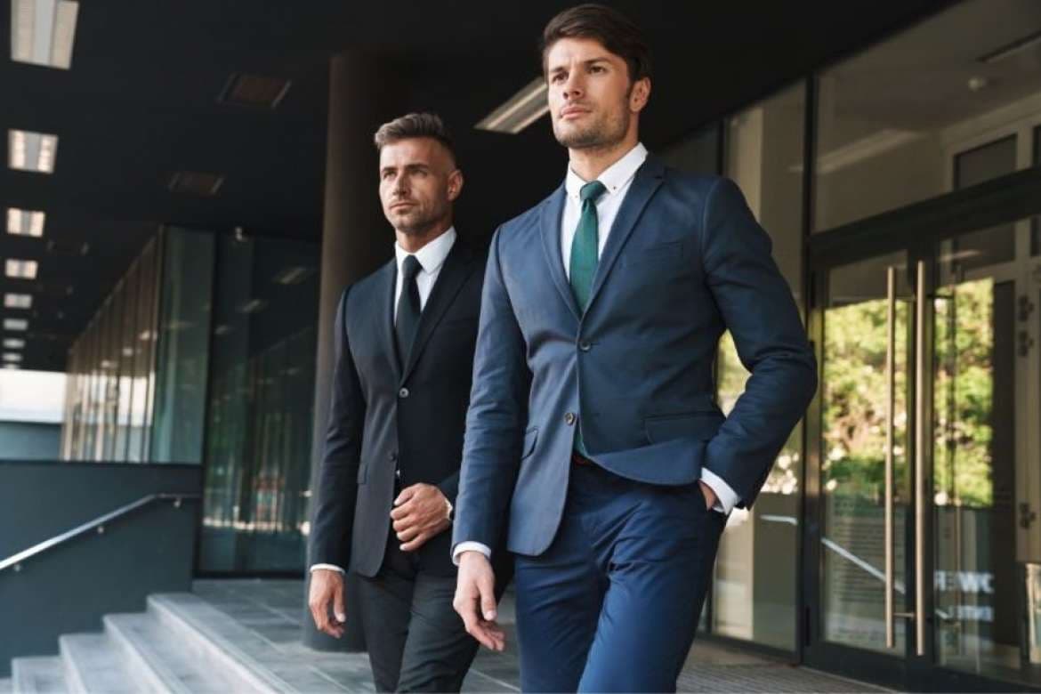 Two men in tailored suits walking outside an office building.