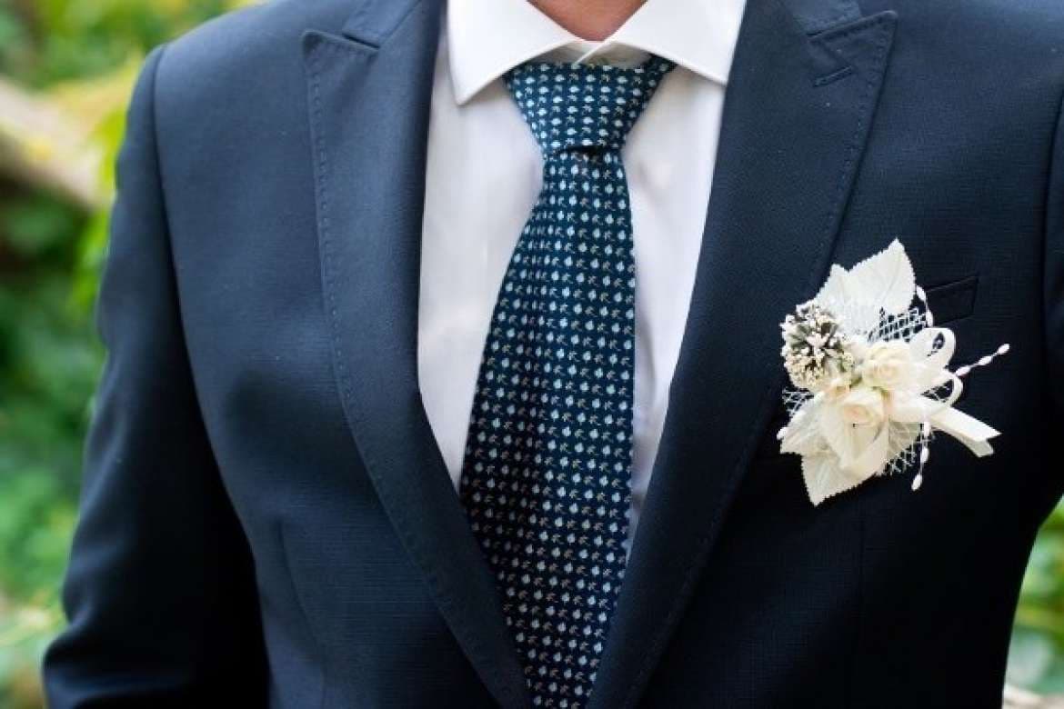 Close-up of a navy suit with a floral boutonniere and patterned tie.