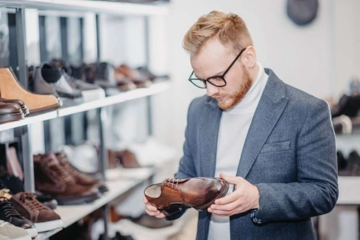 Man in a shoe store examining a brown leather dress shoe.
