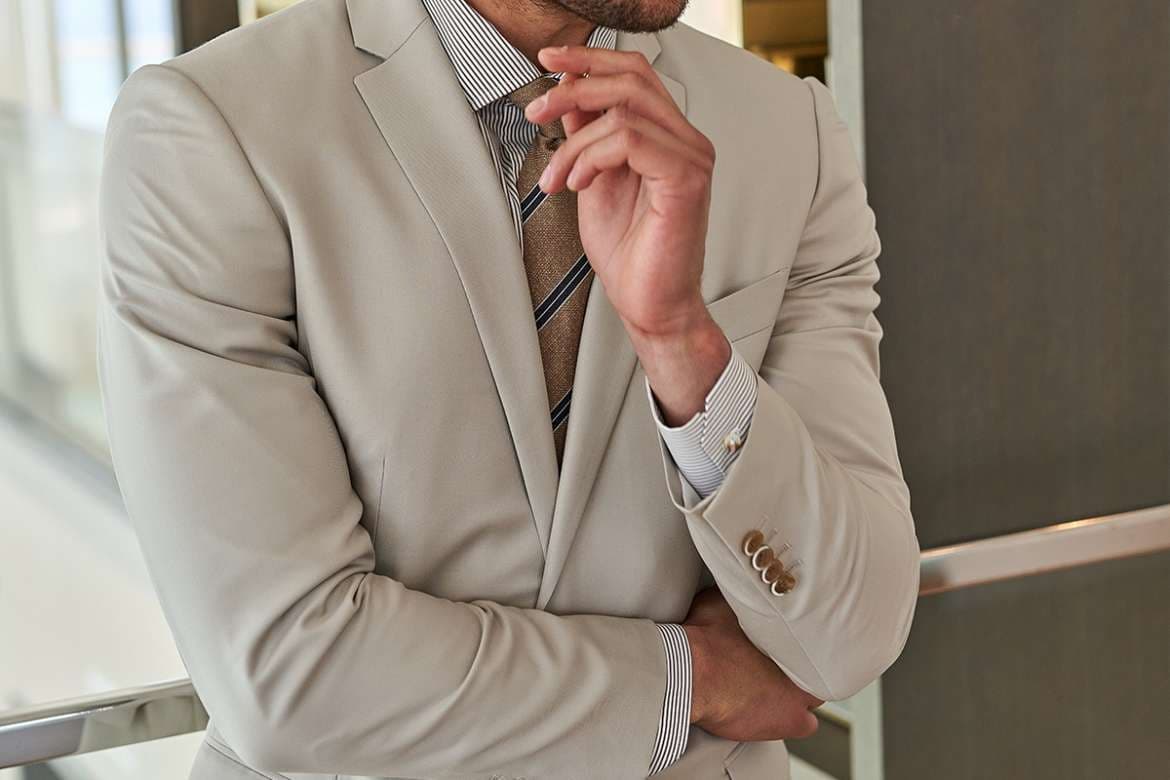 Man in a beige suit with a striped shirt and tie.