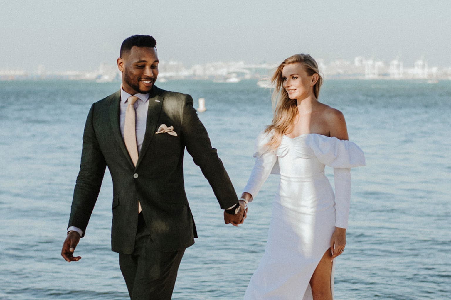 Bride and groom holding hands while walking by the water.
