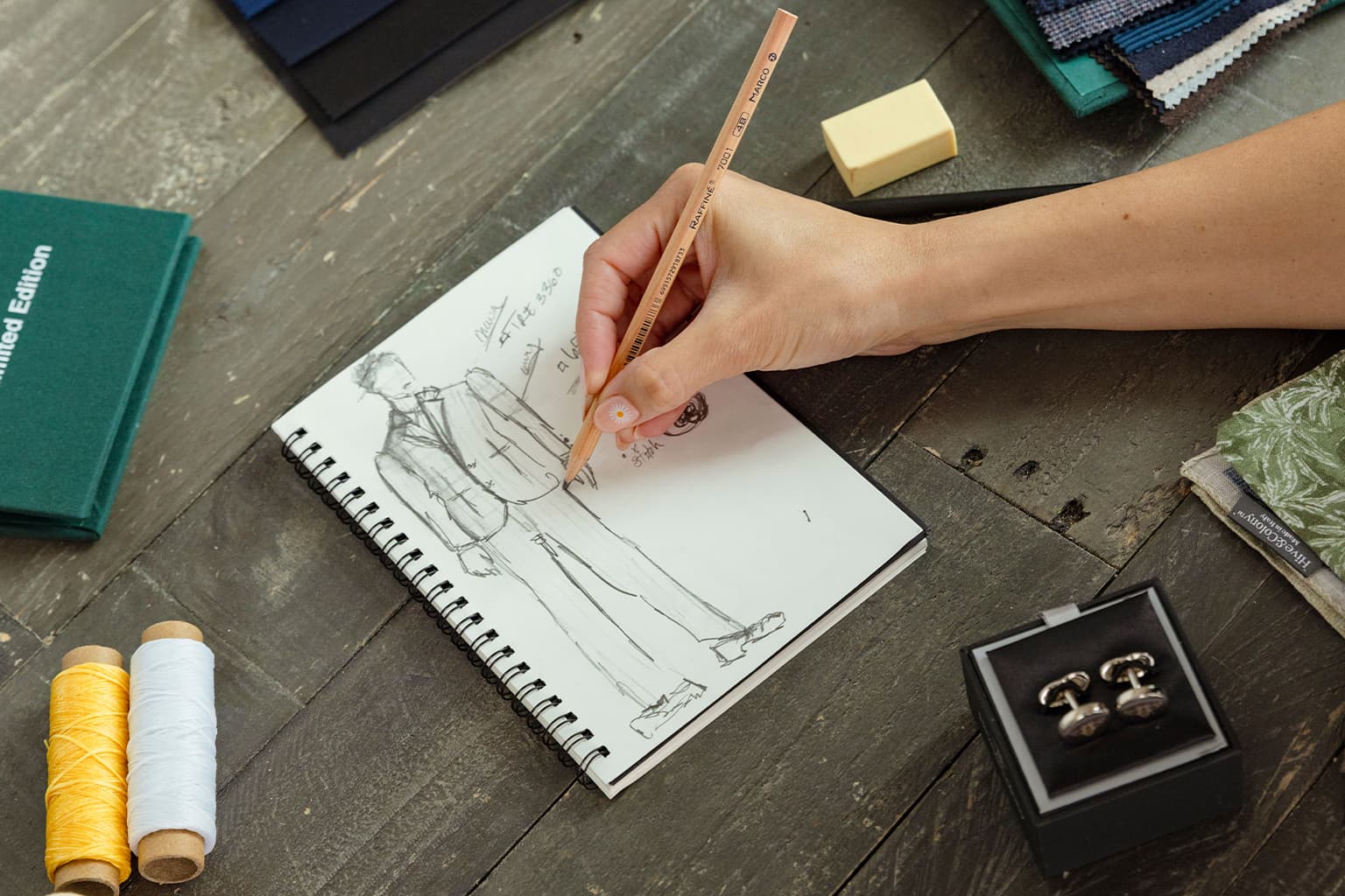 Hand sketching a custom suit design beside tailoring tools.