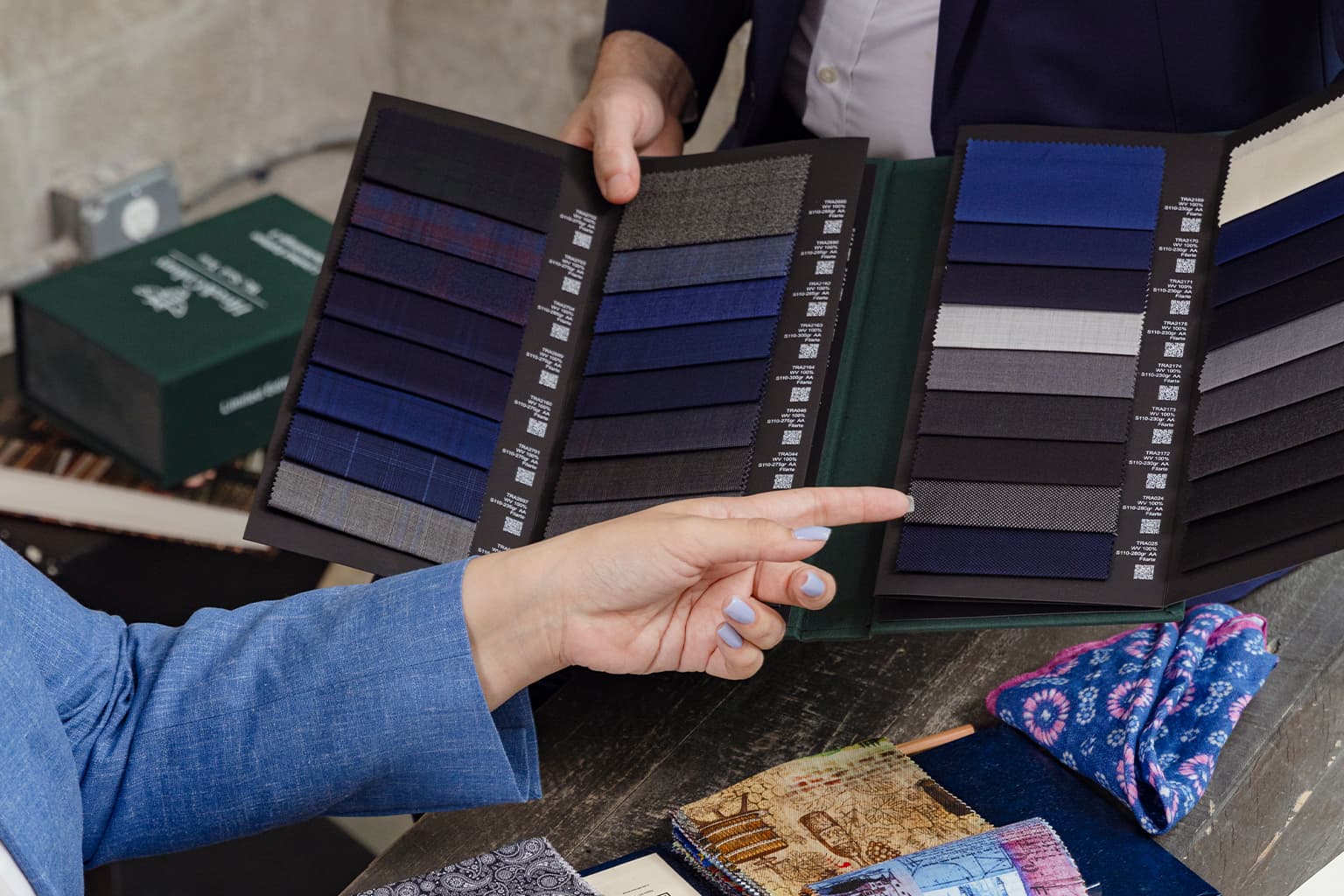 Hands pointing to blue and gray suit fabric swatches.