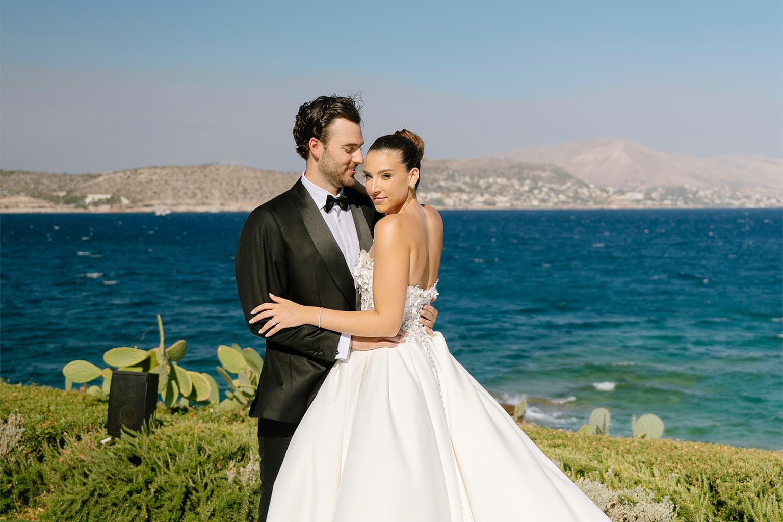 Bride and groom posing together beside the ocean.