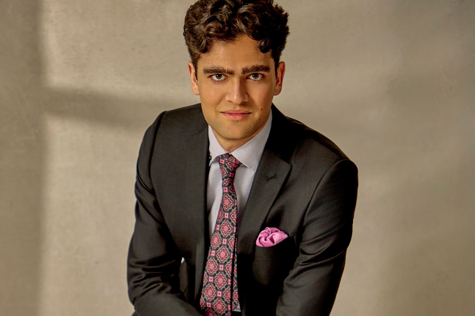 Man in a dark suit with a patterned tie and purple pocket square.