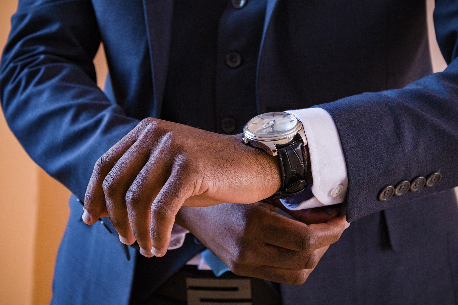 Close-up of a wristwatch worn with a navy suit.