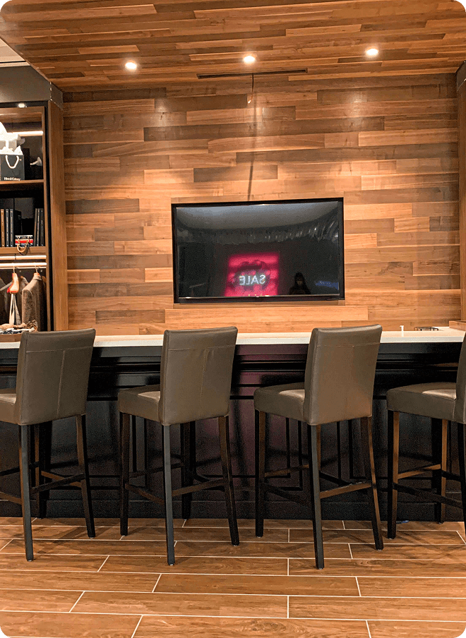 Showroom bar seating in front of a wood wall and wall-mounted screen.