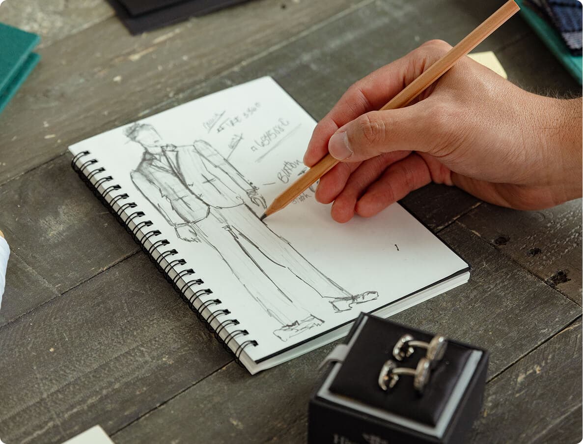 Hand sketching a custom suit design in a notebook.