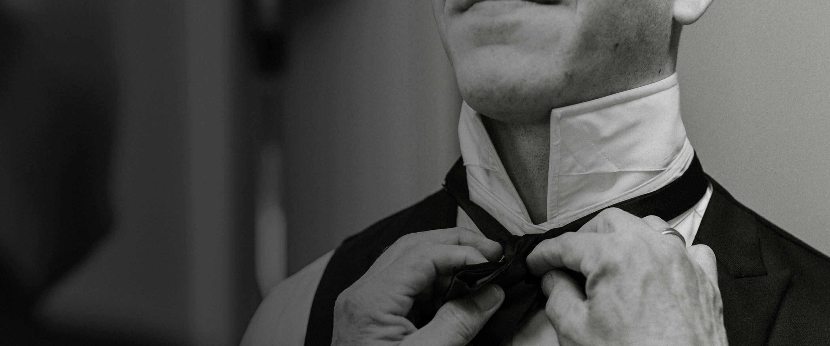 Black-and-white close-up of a groom adjusting his bow tie.