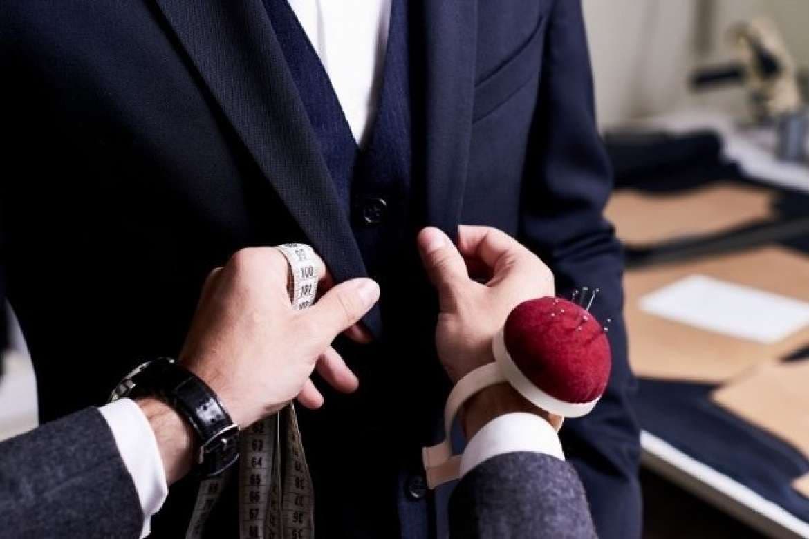 Tailor measuring a navy suit jacket during a fitting.