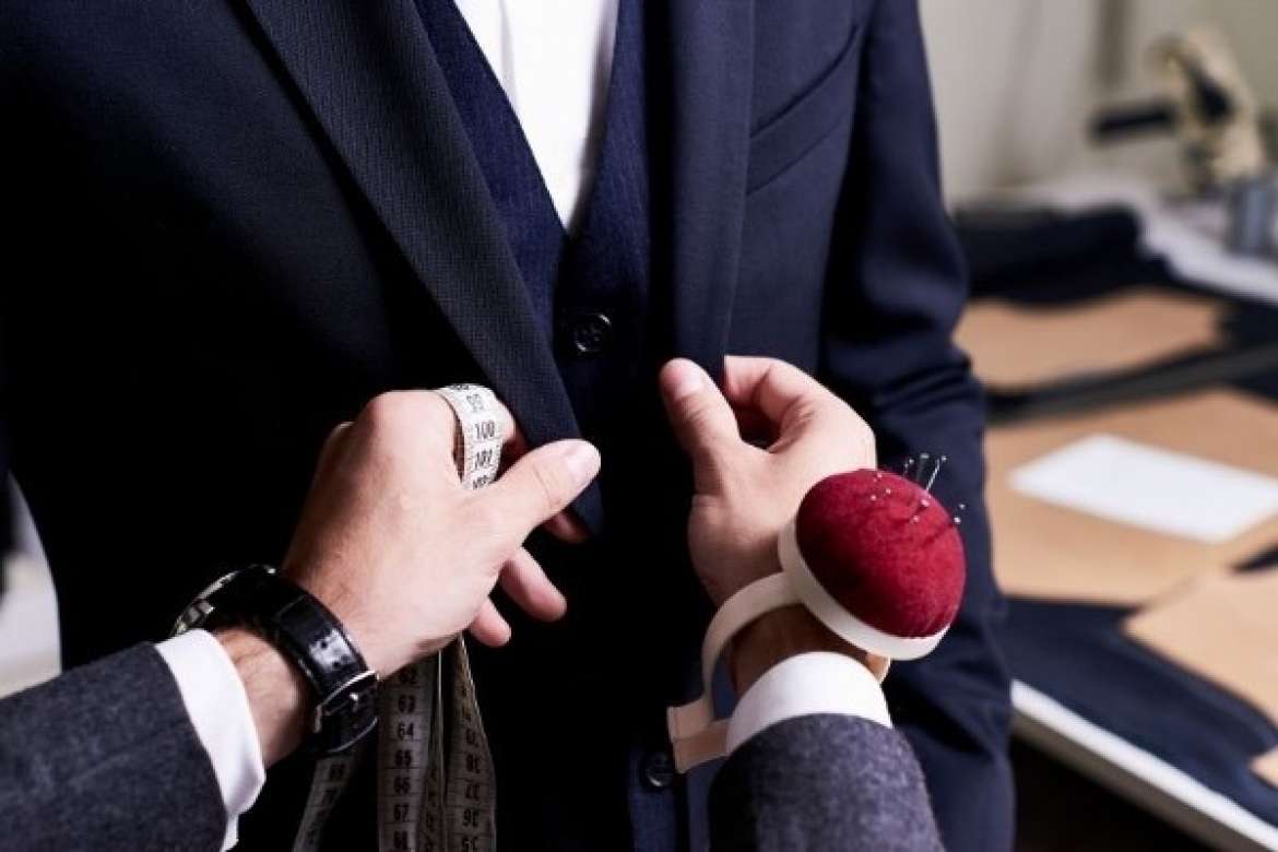 Tailor measuring a navy suit jacket during a fitting.