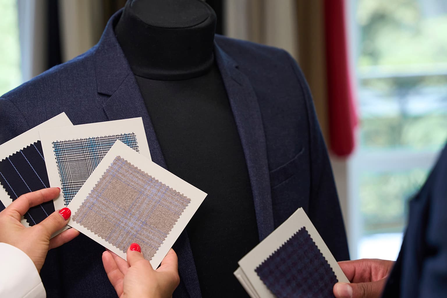 Hands comparing suit fabric swatches beside a navy jacket.