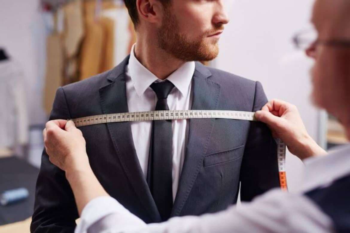 Tailor measuring a man’s chest while he wears a dark suit.