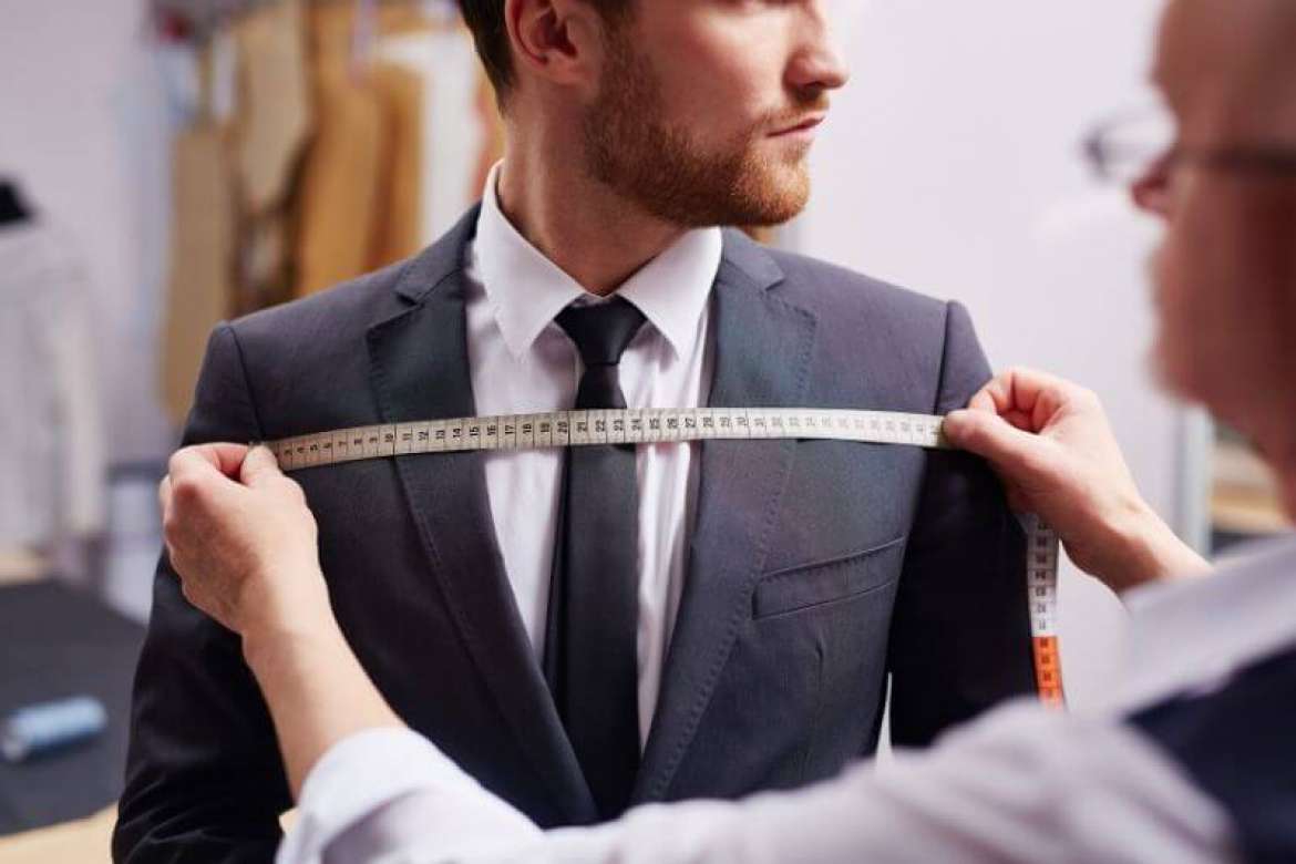 Tailor measuring a man’s chest while he wears a dark suit.