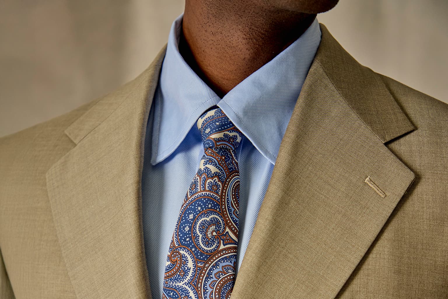 Close-up of a tan suit with a blue paisley tie.
