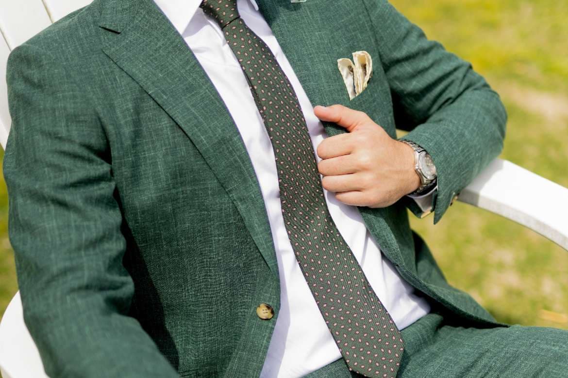 Man seated outdoors in a green suit and patterned tie.