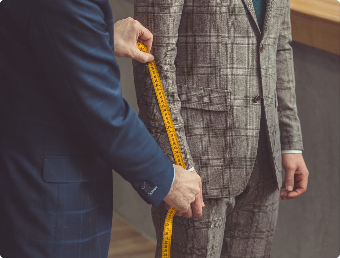 Tailor measuring the sleeve of a gray plaid suit jacket.