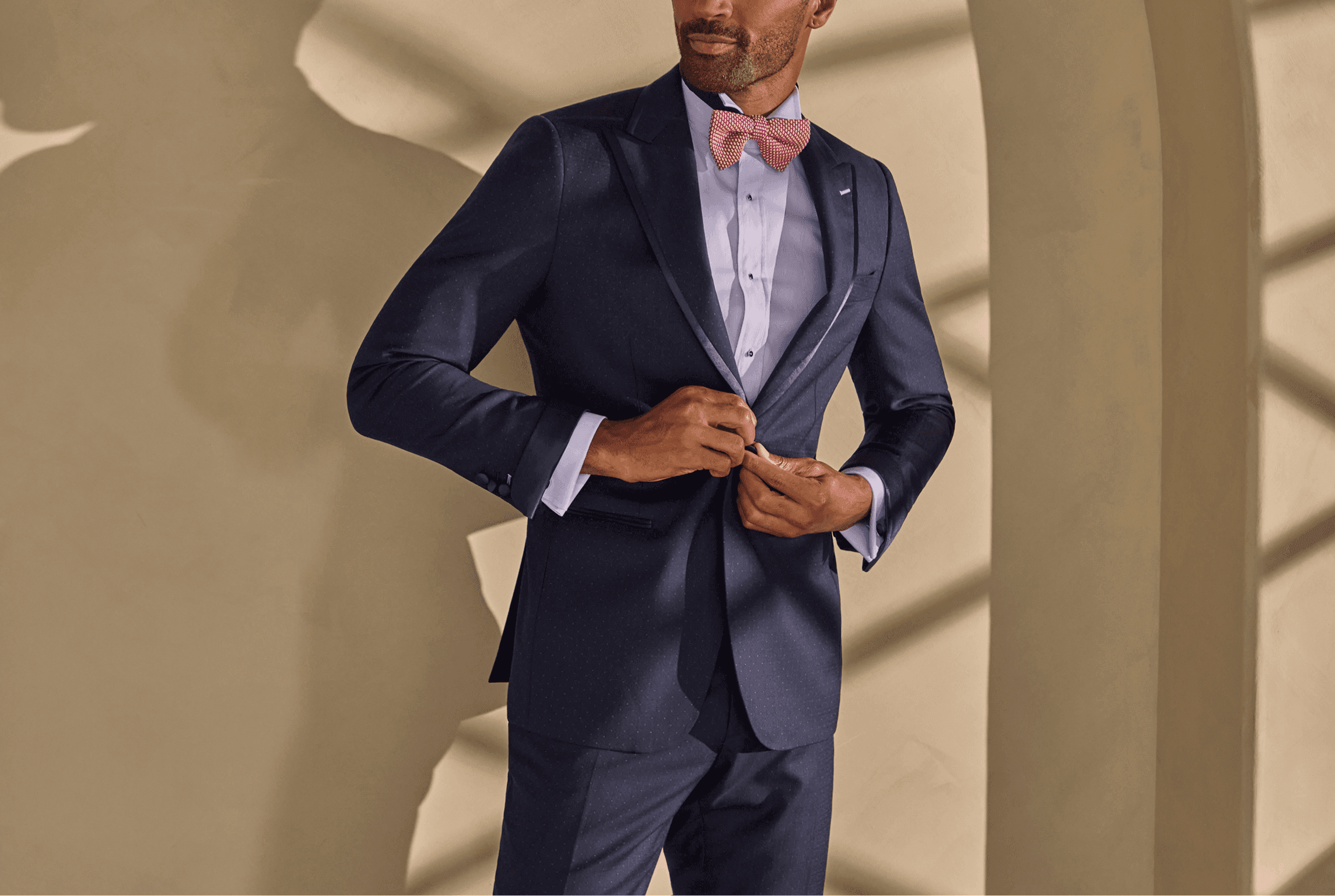 Man buttoning a navy tuxedo with a pink bow tie.