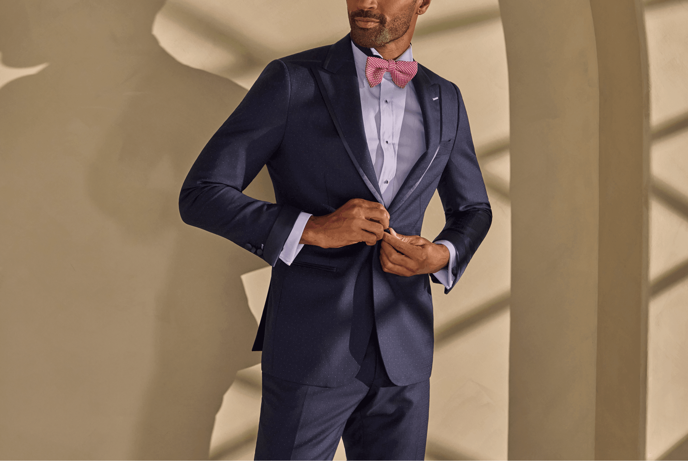 Man buttoning a navy tuxedo with a pink bow tie.
