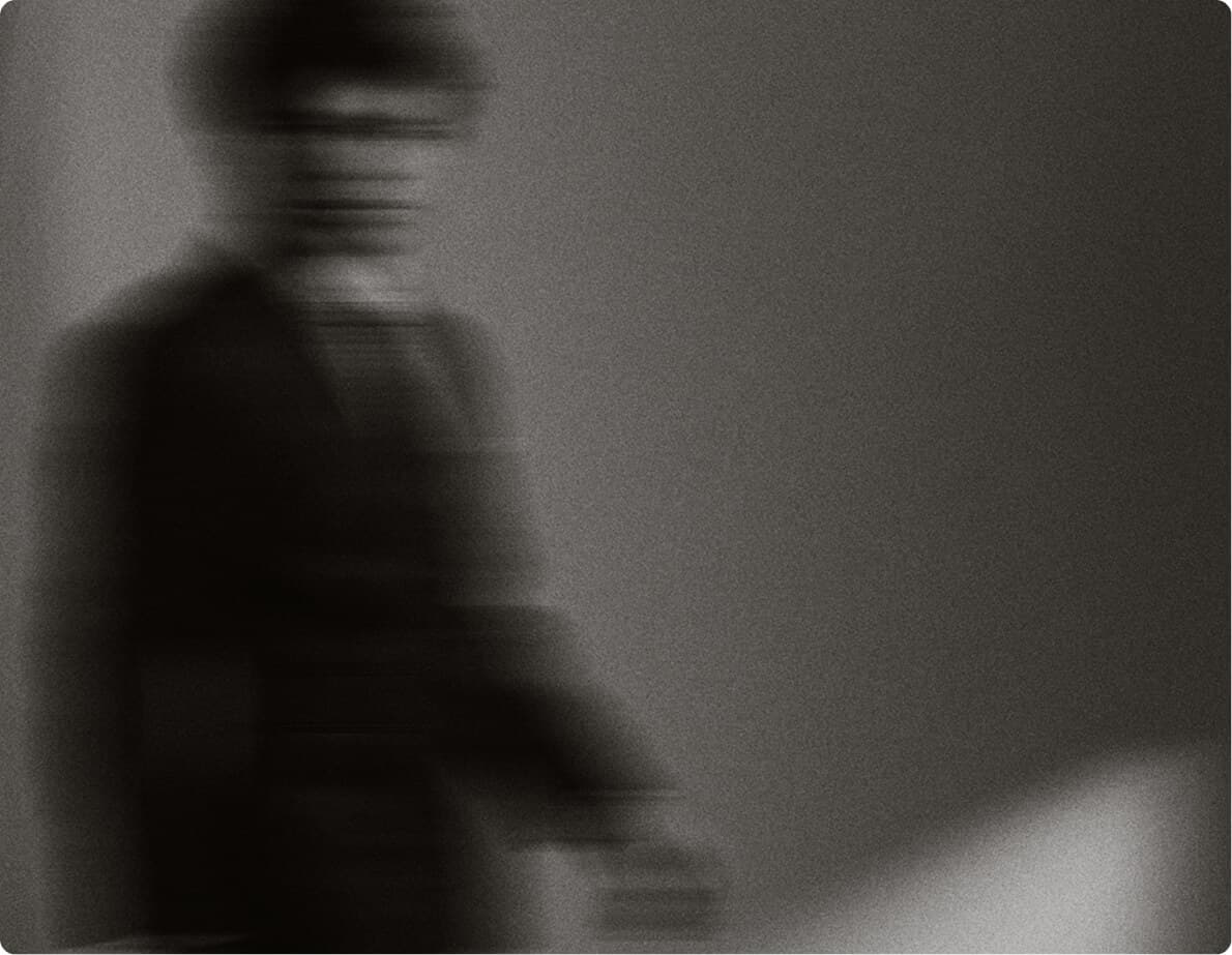 Moody black-and-white blurred portrait of a seated figure.